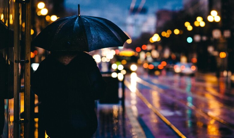 雨の夜の街で傘に顔を隠して立つ人
